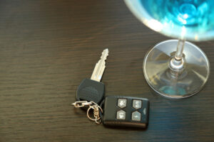 Glass of alcoholic drink and car key, on wooden table